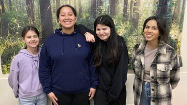 Group of 4 females standing together, smiling for photo