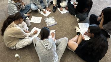 students sitting on floor in a circle, writing on paper